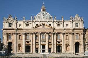 Ornate building in the early morning with a giant order of columns beneath a Latin inscription, fourteen statues on the roofline, and large dome on top.