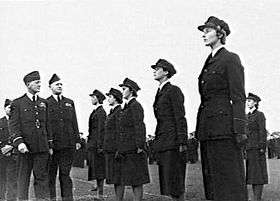 Three men and six women in dark-coloured military uniforms, outdoors