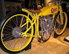 A pristine 1914 motorcycle with a bright yellow frame, racing style handlebars and skinny racing tires.