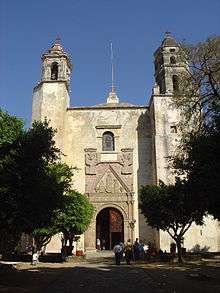 Front of a church with two towers. The portal around the door is decorated with reliefs of two angels, Maria and two other figures.