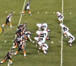 Several American football players in black and white uniforms in action at the mid-field area of the stadium.