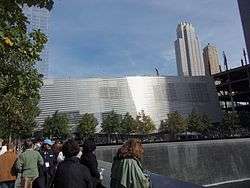 Silver-colored building, with square waterfall in foreground and skyscrapers in background