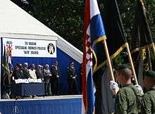 Troops bearing flags standing in front of a podium in a medal presentation ceremony