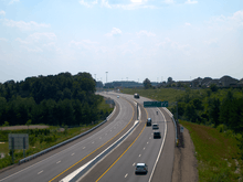 A four lane freeway dives into a ravine and back out, surrounded by rural land on both sides