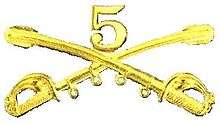 A computer generated reproduction of the insignia of the Union Army 5th Regiment cavalry. The insignia is displayed in gold and consists of two sheafed swords crossing over each other at a 45 degree angle pointing upwards with a Roman numeral 5