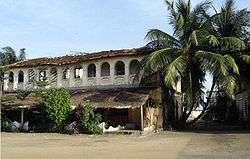 A picture of an old home with large vegetation growing out of it, its structure slightly caving inward.