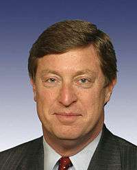 A brown-haired man in his mid forties wearing a black suit and red tie