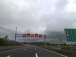 Variable traffic signs placed on a gantry spanning three motorway traffic lanes, indicating slippery pavement and reduced speed limit