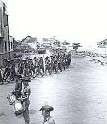 Soldiers marching under arms with rifles at the slope file past a drum band