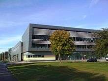 A contemporary building constructed with glass and steel with silver and coloured cladding set in mature landscape