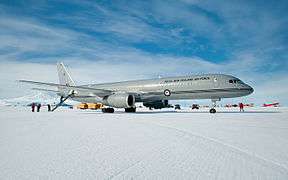 Gray twinjet stationary on ice, with aft stairs and surrounding personnel.