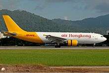 An aircraft painted in white colour with the name Air Hong Kong painted in red on the fuselage, and in yellow colour from the rear to the tail with the name DHL painted in red on the tailfin.