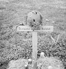 Wooden cross on grave with a steel helmet on top of cross