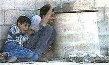 Man and a boy crouching behind a concrete drum; the man is waving