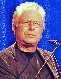 Photo of a male with balding white hair. He is wearing a black jacket.