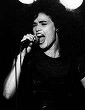 Black and white image of a woman with her eyes closed and mouth open, holding a microphone.