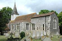 A flint church with a red tied roof and a tower at the west end, seen from the southeast