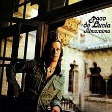 Man in denim jacket standing in a doorway leading into a hacienda courtyard.