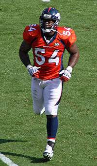 Andra Davis, a six-foot-one African-American man, jogs to the football sideline in the orange, white and navy uniform of the Denver Broncos, circa 2009.