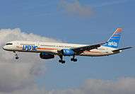 Side view of twinjet airliner in flight, with several clouds behind.