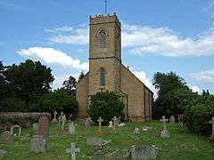 Stone building with prominent square tower. In the foreground are gravestones.