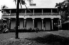 Photograph of a two-story building with broad verandas in a tropical setting