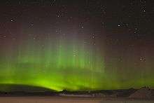 A swirling green glow in the night sky above snow-covered ground