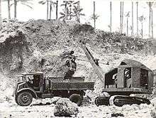 Black and white photo of a mechanical digger dropping soil into the tray of a truck