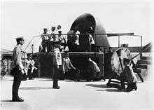 A large gun encased in an open backed metal turret atop a fort.