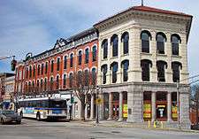 A row of brick buildings with continuous decorative white trim at the roof seen from an oblique angle across the street. At the right, closer to the camera, is a stone building with arched windows and a red tiled roof. The words "Ossining National Bank" are carved into the stone near the roof