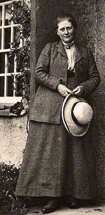 Black-and-white photo of a woman in a dress standing.