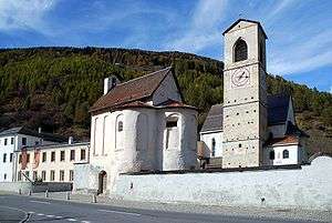 A clock tower standing beside two small houses and a museum.