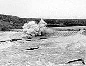 View of an explosion atop a dam in a flooding river