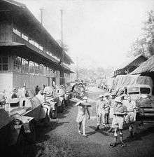 Soldiers move between military vehicles next to a building