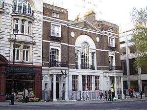 the facade of a three-story Georgian building in London. The building is in brown-red brick, with cream-coloured Portland stone edging, portico and columns