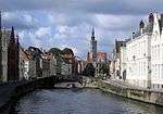 A small motorboat rides under a bridge over a canal, which runs between several buildings.