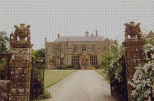 Yellow stone building at the end of a driveway accessed via stone gateposts.