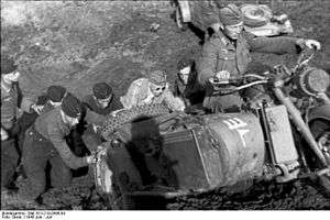 a black and white photograph of a group of soldiers pushing a motorcycle combination up a hill