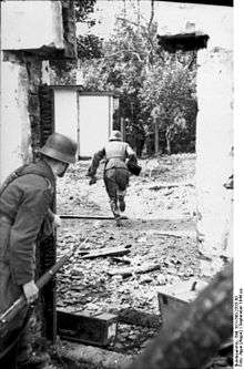 One man running across open space while a second peeps around a doorway