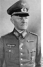 A man wearing a peaked cap, military uniform with an Iron Cross displayed at the front of his uniform collar.