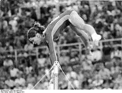 woman above a bar holding onto it during a gymnastics routine