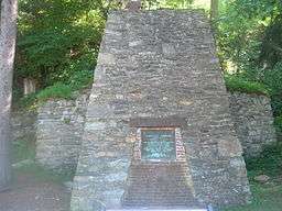 A fieldstone iron furnace with a metal plaque reading "Caledonia Furnace, erected 1837 by Thaddeus Stevens" and more text too small to read. There are trees in the background