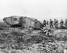 Group of armed soldiers march past a wrecked tank and a body