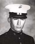 Head of a young white man wearing a white peaked cap with black visor and a dark military jacket.