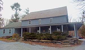 A wooden blue house with a wing on the left and a verandah around the middle and right