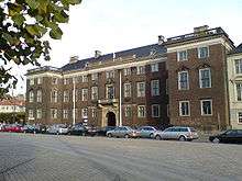 Three story palace with two large wings.  Many decorative elements such as cornices, window pediments, and a stone balcony over the entrance.