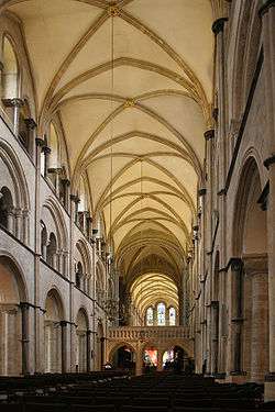 Interior view of a tall long building. The roof is light colored with darker arches providing support for the stonework. The walls are in three layers, each layer consisting of a set of arches.