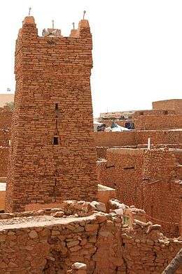 A picture of a tall stone and medieval looking tower, surrounded by buildings constructed with the same material.