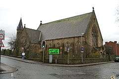 A small stone church with a transept and an octagonal bell turret with a conical roof