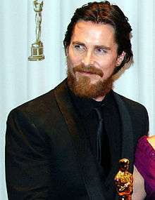 Christian Bale is smiling to his right.